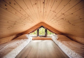 Gemütliches Dachzimmer in einer Lodge mit Holzverkleidung, zwei Einzelbetten und Fenster mit Ausblick.