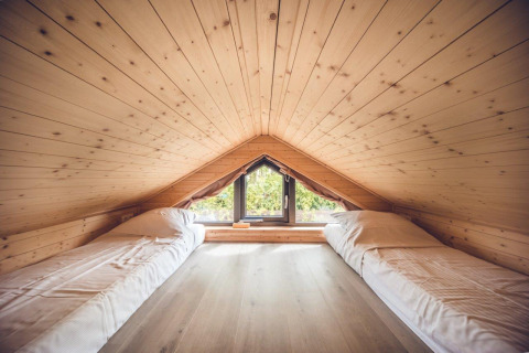 Ático acogedor en un refugio, con paneles de madera, dos camas individuales y ventana con vista exterior.