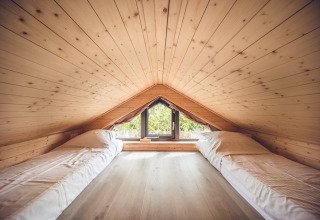 Cozy attic lodge room with wood paneling, two single beds, and a window overlooking green scenery.