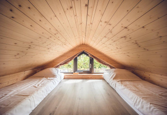 Ático acogedor en un refugio, con paneles de madera, dos camas individuales y ventana con vista exterior.