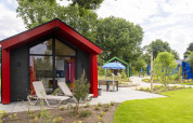 Modern hunting chalet at Holiday Park Ackersate, Netherlands, with lounge chairs and lush green surroundings.