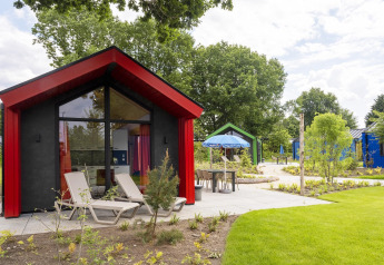 Modern hunting chalet at Holiday Park Ackersate, Netherlands, with lounge chairs and lush green surroundings.