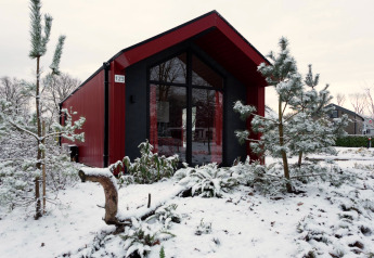 Rotes Jagdchalet im Holiday Park Ackersate, Niederlande, umgeben von verschneiten Kiefern im Winter.