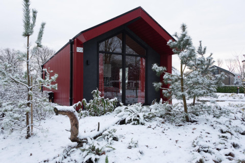 Red hunting chalet at Holiday park Ackersate, Netherlands, surrounded by snow and pine trees in winter.