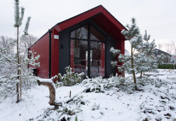 Red hunting chalet at Holiday park Ackersate, Netherlands, surrounded by snow and pine trees in winter.
