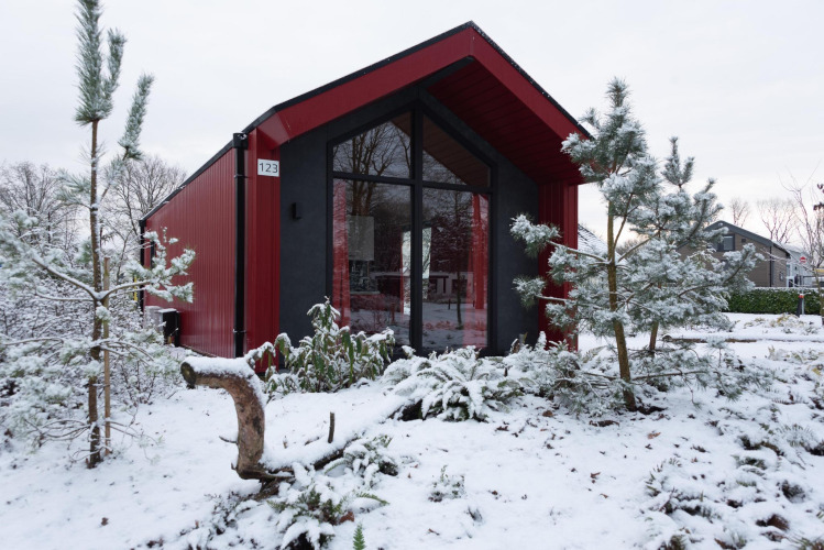 Rotes Jagdchalet im Holiday Park Ackersate, Niederlande, umgeben von verschneiten Kiefern im Winter.