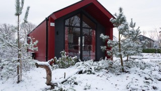 Chalet da caccia rosso all'Holiday park Ackersate, Paesi Bassi, circondato da neve e pini in inverno.