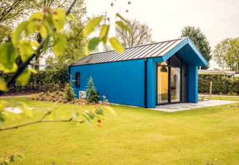 Blaues Jagdchalet im Holiday Park Ackersate, Niederlande, umgeben von Wiese und Bäumen im Frühling.