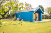Blå jagthytte ved Holiday park Ackersate i Holland, omgivet af grønt græs og træer en solrig dag.