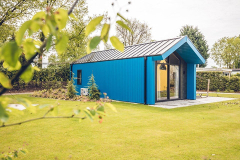 Blauw jachthutje op vakantiepark Ackersate in Nederland, met gras en bomen op een zonnige lentedag.
