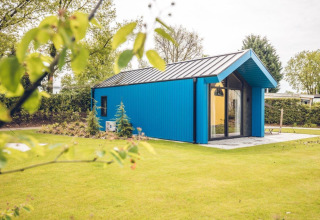 Blauw jachthuisje op vakantiepark Ackersate in Nederland, omgeven door gras en bomen op zonnige dag.