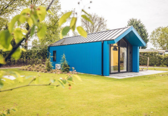 Blauw jachthuisje op vakantiepark Ackersate in Nederland, omgeven door gras en bomen op zonnige dag.