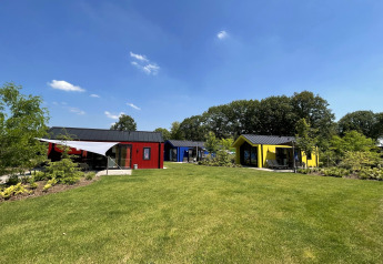 Bunte Jagdhütten im Holiday Park Ackersate, Niederlande, mit grüner Wiese und blauem Himmel.