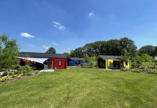 Colorful hunting chalets at Holiday Park Ackersate in the Netherlands, set among grassy lawns and trees.