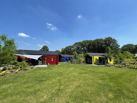 Kleurrijke jachthutten in Vakantiepark Ackersate, Nederland, met grasvelden en een stralende lucht.