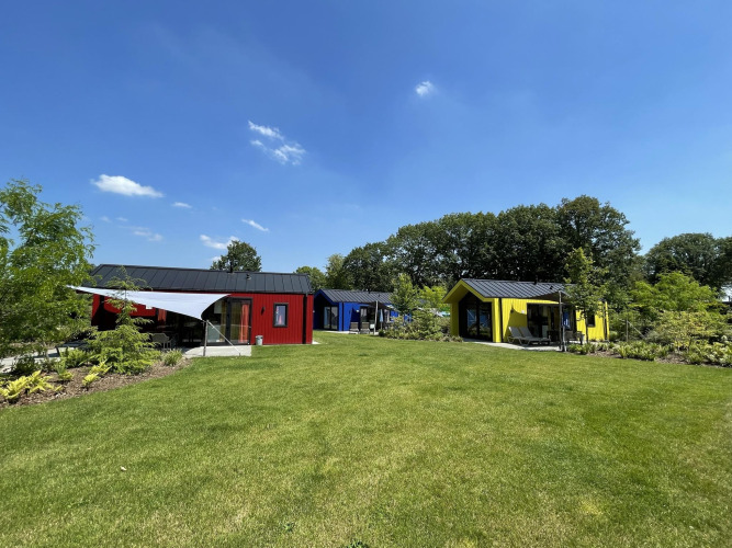 Bunte Jagdhütten im Holiday Park Ackersate, Niederlande, mit grüner Wiese und blauem Himmel.