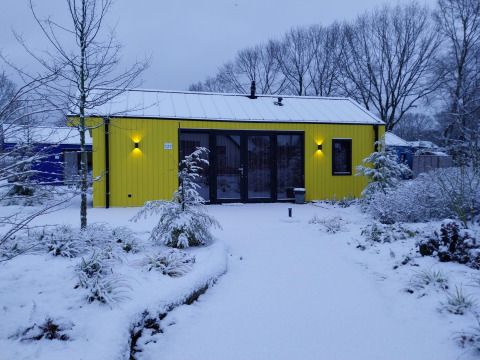 Chalet di caccia giallo al Holiday Park Ackersate nei Paesi Bassi, circondato dalla neve e piante invernali.