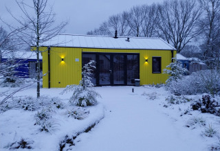 Chalet di caccia giallo al Holiday Park Ackersate nei Paesi Bassi, circondato dalla neve e piante invernali.