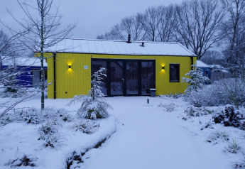 Jachthut bij Holiday park Ackersate in Nederland, geel geschilderd en omringd door sneeuw en winterplanten.