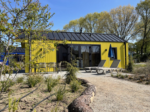 Yellow hunting chalet at Holiday Park Ackersate, Netherlands, patio with loungers and umbrella outside lodge.