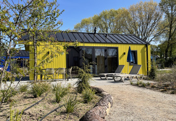 Chalet de caza amarillo en Holiday park Ackersate, Países Bajos, con tumbonas y sombrilla en la terraza.