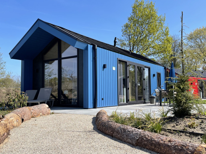 Blaues Jagdchalet im Holiday park Ackersate, Niederlande, modernes Gebäude mit Terrasse im Grünen.