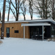 Moderne Forest Villa lodge in de sneeuw bij Vakantiepark Ackersate, Nederland, omgeven door hoge bomen.