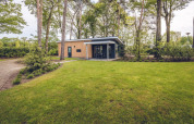 Forest Villa lodge nel parco vacanze Ackersate, Paesi Bassi, circondata da alberi e prato verde.