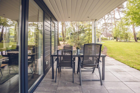 Terraza con mesa y sillas en Forest Villa, Holiday park Ackersate, Países Bajos, rodeada de naturaleza verde.
