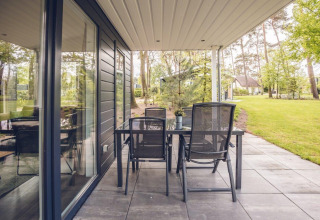Terraza con mesa y sillas en Forest Villa, Holiday park Ackersate, Países Bajos, rodeada de naturaleza verde.