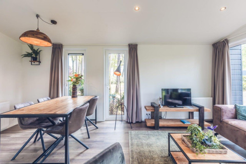 Lyst og moderne opholdsområde i Forest Villa på Holiday park Ackersate, med spisebord, tv og store vinduer.