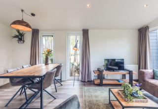 Lichte, moderne woonkamer in Forest Villa op Holiday park Ackersate, Nederland, met eettafel en tv.