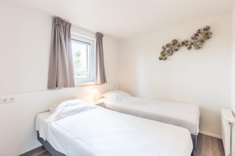Helder vertrek met twee enkele bedden, raam en wandkunst in Forest Villa, Holiday park Ackersate, Nederland.