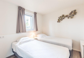 Helder vertrek met twee enkele bedden, raam en wandkunst in Forest Villa, Holiday park Ackersate, Nederland.