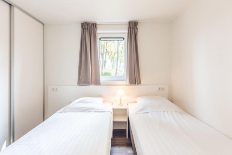 Dormitorio luminoso con dos camas individuales y ventana en Forest Villa en Holiday park Ackersate, Países Bajos.