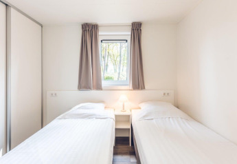 Dormitorio luminoso con dos camas individuales y ventana en Forest Villa en Holiday park Ackersate, Países Bajos.