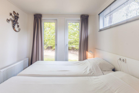Dormitorio con dos camas individuales en Forest Villa, Holiday park Ackersate, Países Bajos, vista a árboles.