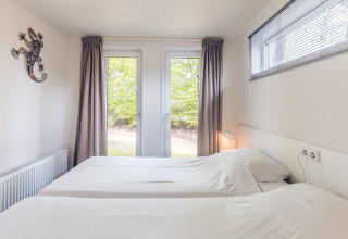 Dormitorio con dos camas individuales en Forest Villa, Holiday park Ackersate, Países Bajos, vista a árboles.