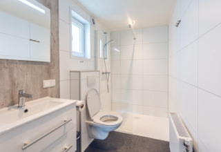 Baño moderno con inodoro, lavabo y ducha en Forest Villa del Holiday park Ackersate, Países Bajos.