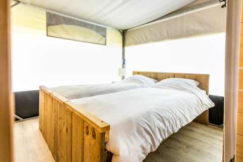 Vista interior de una cómoda cama con marco de madera en una tienda safari Tentvilla en De Witte Berg, Países Bajos.