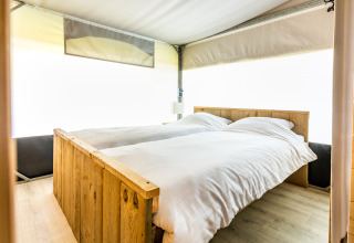 Interieur van een comfortabel bed met houten frame in een Tentvilla safaritent op De Witte Berg vakantiepark.