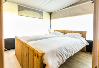 Interieur van een comfortabel bed met houten frame in een Tentvilla safaritent op De Witte Berg vakantiepark.