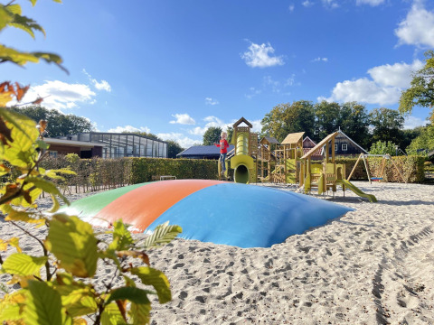 Aire de jeux avec coussin gonflable, toboggans et structures de grimpe sur un site de glamping ensoleillé.