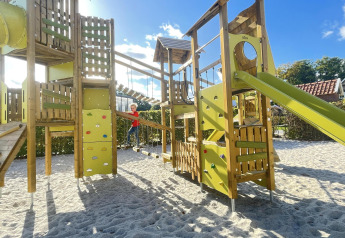 Grande area giochi con struttura da arrampicata e scivolo, fotografata in un alloggio glamping.