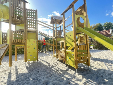Large playground with climbing structure, slide, and child playing, photographed at a glamping site.
