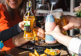 Venner skåler med forskellige drikkevarer og nyder mad på en restaurant under et glampingophold.