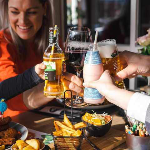 Vrienden klinken met drankjes en eten samen in een restaurant tijdens een glampingverblijf.