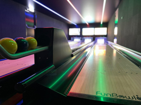 Boules de bowling colorées et piste éclairée, photographiées dans un espace loisirs d'un hébergement glamping.