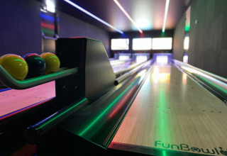 Verlichte bowlingbaan met kleurrijke ballen, vastgelegd in een recreatieruimte van een glamping accommodatie.