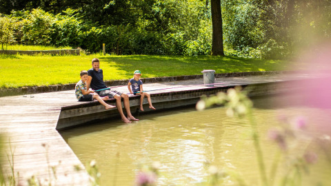 Famille assise sur un quai en bois près de l'eau au parc De Witte Berg, Pays-Bas, par temps ensoleillé.